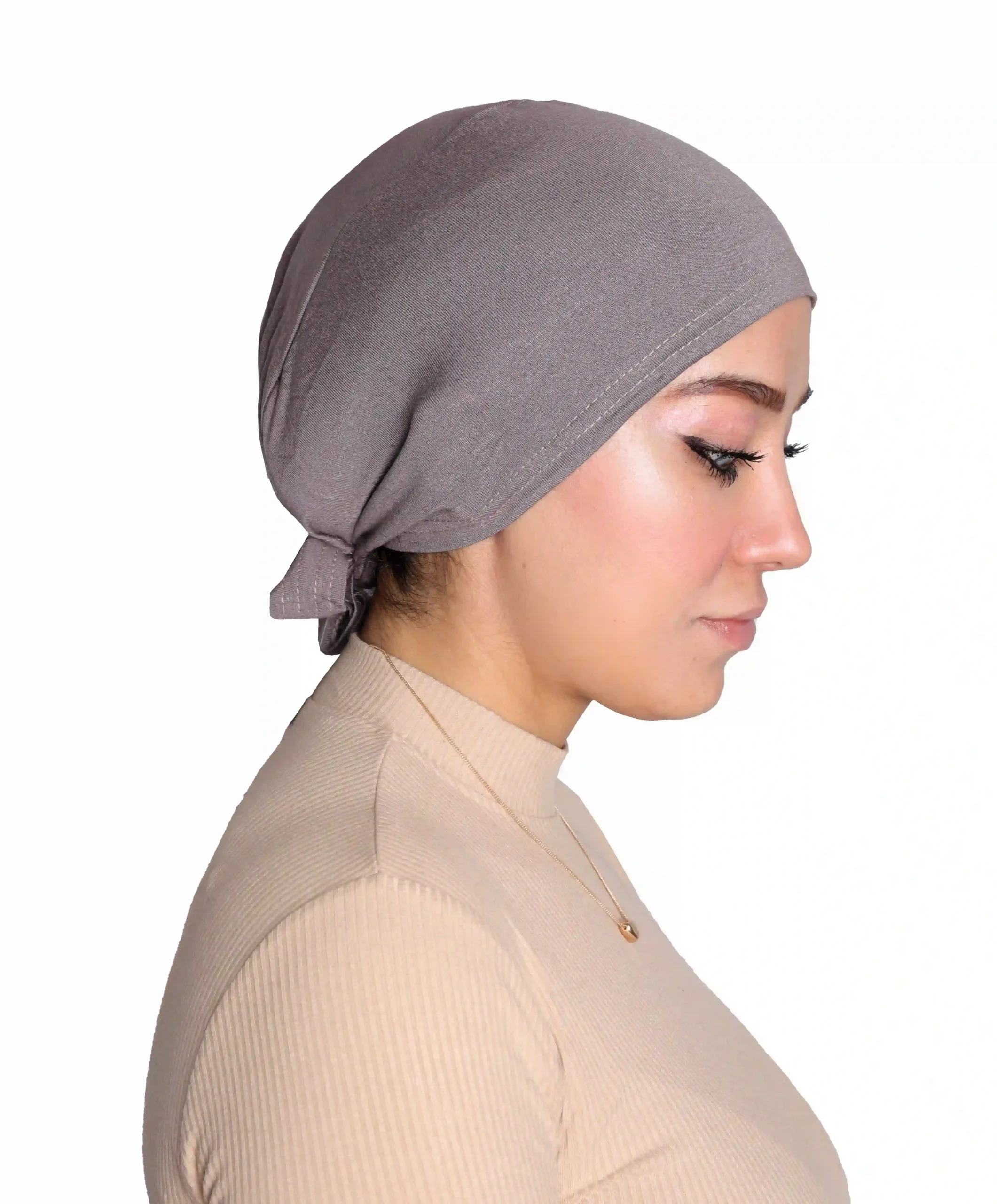 A woman models a Chic Grey Turban Cap for Women, shown in a profile view with a hand near her chin, emphasizing the tidy tie-back detail and smooth silhouette.