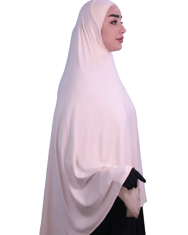 A woman modeling a luxurious fawn beige cotton hijab, smiling directly at the camera, showcasing the complete look of the garment.