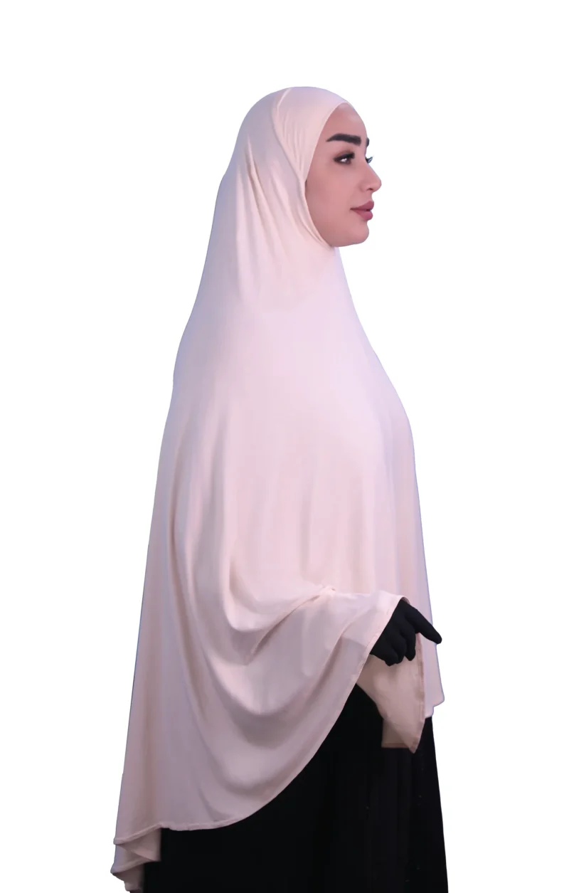 A woman modeling a luxurious fawn beige cotton hijab, smiling directly at the camera, showcasing the complete look of the garment.