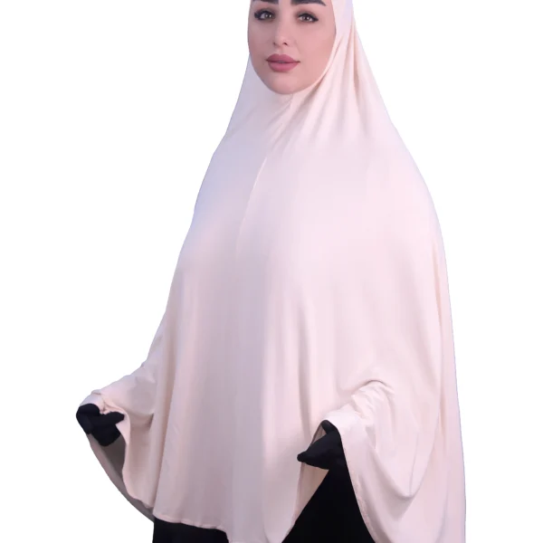A woman modeling a luxurious fawn beige cotton hijab, looking directly at the camera with her hands slightly out, highlighting the full coverage and comfortable fit.