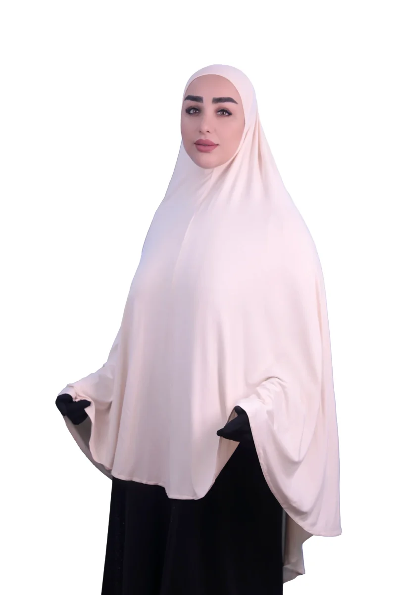 A woman modeling a luxurious fawn beige cotton hijab, looking directly at the camera with her hands slightly out, highlighting the full coverage and comfortable fit.