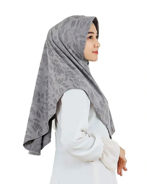 A woman models a Chic Grey Hijab with Leaf Pattern, viewed from the side, showcasing the comfortable fit around the face and the texture of the leaf-patterned fabric.