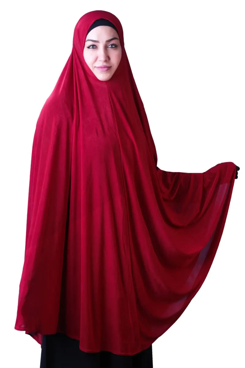 A woman models a stylish Red Satin Hijab for Women, standing at an angle while holding up the side of the flowing fabric to emphasize the material and volume.